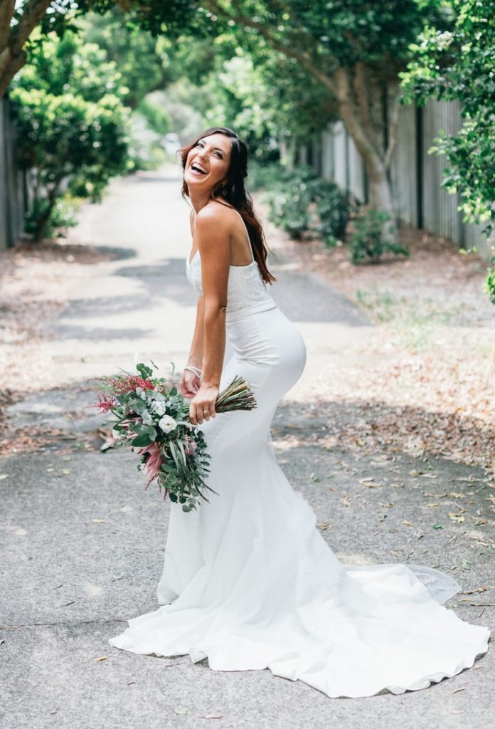 Gold Coast bride laughing in flowing gown with bouquet